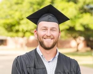 Grant Mitzelfelt smiles wearing his graduation cap 和 gown.
